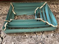 Top view of the large, square, accordion metal lampshade showing its turquoise color and white straps holding the pleats.