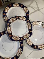 Photo showing set of four plates with cobalt blue and gold floral border, including three round and one square plate