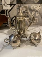 Photo showing all three silver plate tea set pieces: teapot, sugar bowl with lid, creamer, arranged on a countertop.