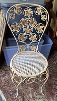 Front view of vintage wrought iron chair showing gold finish and floral cutout design on the backrest with perforated seat.