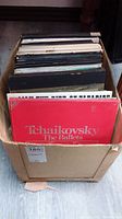 Cardboard box filled with multiple vinyl LP albums, the most visible has a red cover labeled Tchaikovsky The Ballets.