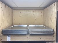 Stack of metal baking sheets on a wooden shelf, showing two distinct designs of trays.