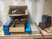 Full lot showing stacked boxes with joist brackets, metal hardware, heavy bench vice, black space heater, blue nylon rope coil, paintbrush, and a large metal cutting tool with red handle.