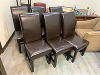 Six dark brown vinyl-covered dining chairs with wooden legs arranged in two rows on a wooden floor.