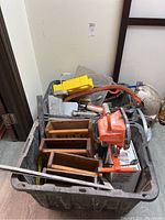 Two bins filled with various construction hand tools, including saws, rulers, work lights, drywall tools, sealants, hammers, a watering can, and a cast iron pipe.