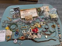 Photo showing entire lot spread on a table including boxed items, plastic bags with bead strands, various bracelets, necklaces, brooches, and pins.