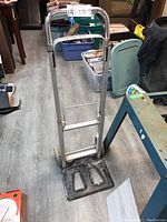 Metal dolly with handle and wheels shown on floor with surrounding items.