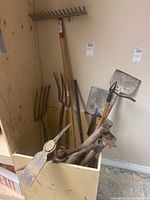 Photo shows two pitchforks, a square shovel, part of an axe, and other tools in a wooden enclosure.