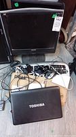 Dell computer monitor, black, shown with keyboards, mice, and Toshiba laptop on floor, cables tangled