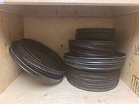 Photo of stacked metal pizza pans inside a wooden crate, showing multiple pans piled on each other with visible wear and dirt.
