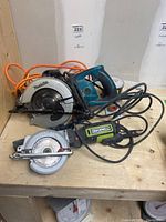 Two corded circular saws (Makita and Rockwell), orange extension cord and Neptune pressure gauge on a wooden surface.