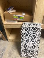 Three boxes of porcelain tiles stacked, showing patterned tile packaging and some tile spacers on top