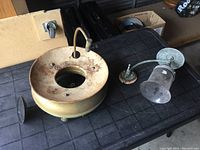 View of two antique gas light fixtures showing a round brass fixture and a curved metal arm with glass shade on a dark table surface.