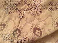 Close-up photo of the antique hand made Quaker linen table cloth showing floral and geometric lace detail with embroidery on off-white fabric.