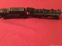 Side view of antique black metal train engine connected to coal tender car on red background.