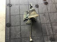 Cast iron bird bell hanging with chain and round weight at bottom, showing overall item.
