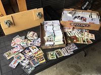 Wide view of mixed sports cards in boxes and loose on a table showing the quantity and variety in the lot.