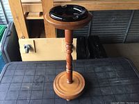 Wide view showing entire wooden ashtray stand with black glass ashtray set on top and the smooth round base.