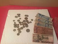 Overall lot showing small foreign coins scattered next to a stack of Mexican peso banknotes on a white surface.