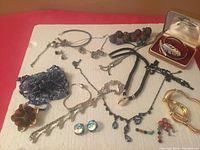 Overview image showing all vintage jewelry pieces arranged on a white fabric surface including necklaces, bracelets, earrings, brooches, and a boxed feather brooch