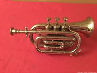Full side view of silver miniature trumpet on red background