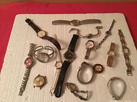 Overview of 15 assorted vintage watches laid on white background showing various cases, bands, and dial colors.