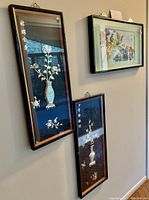 Three framed Asian wall art pieces displayed on wall, two vertical floral embroidery style and one horizontal colorful bird painting/print.