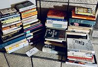 Photo showing multiple stacks of assorted books arranged on an outdoor surface. Titles include history, finance, self-help, and biography genres.