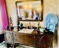 Wide angle photo of wood buffet with decorative objects on top and ornate mirror hanging above.