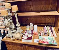 Full view of the candle holders with candles, various loose candles, potpourri containers, and decorative glass tray arranged on wooden shelf surface