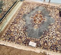 Photo showing 4 feet x 6 feet area rug with intricate medallion design in shades of gray, beige, and brown, featuring fringe
