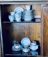 Full set displayed on wooden shelf including stacked plates, cups, saucers, and sugar bowl with lid.