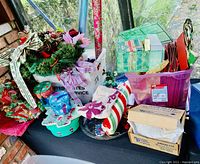 Front angled view showing an assortment of Christmas wrapping paper rolls, gift boxes, and decorative greenery on a table near a window