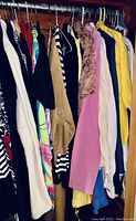 Photo of mixed women's tops including sweaters and blouses in various colors and patterns hung on a wooden rod.