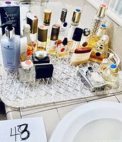 Multiple assorted fragrance bottles displayed on a clear patterned tray on a tiled countertop.