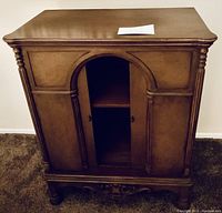 Photo of vintage wooden console cabinet showing front view with arched double doors, carved side pillars, and carved bottom trim.