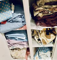 Shelves holding folded king size bed sheets and pillow cases mostly in blue, beige, brown and floral patterns.