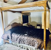 Photo showing king size wooden canopy bed with upholstered headboard and white fabric canopy. Bedspread is a brown quilted fabric. Bed frame and posts are wooden with carved details.