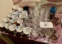 Overall shot showing many white coffee cups and an assortment of clear and tinted drinking glasses arranged on a tray.