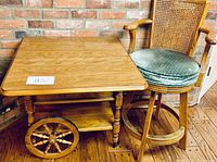Wooden serving cart with two large spoked wheels and two shelves, alongside wooden bar stool with upholstered seat and caned backrest.
