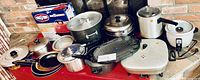 Photo showing various pots, pans, electric skillet, rice cooker, steamer, and grills arranged on a table.