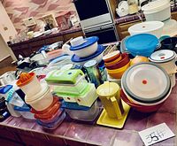 Overview of assorted kitchenware on table, showing plastic bowls, containers with lids, orange juicer, and various other items from the lot.