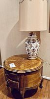 Porcelain floral patterned lamp on a wooden end table with drawers and carved legs, showing wood grain top and drawer detail.