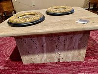 Square marble table with two round decorative mirrors on top, placed on red oblong rug with textured pattern