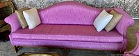 Front view of pink silk fabric mid-century sofa with 3 accent pillows (white and beige). Furniture placed on carpeted floor.
