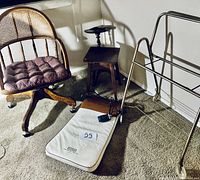 Photo showing the mid-century wooden chair with woven cane backrest, electric massager pad on floor with remote, small wooden stand, and metal rack.