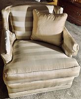 Close-up photo of the silk-upholstered armchair in beige striped fabric with a large square pillow on the seat.