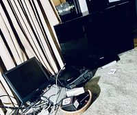 Floor shot showing Toshiba flat screen TV, black LCD monitor, digital video recorder, VHS player and basket of cables