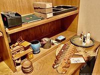 Wooden carved pineapple split in half, three wooden trays, broken wooden miniature desk, blue ceramic pot, other small sculptures and decorative boxes on wooden shelf