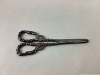 Ornate antique grape shears with detailed sterling silver handles, laid flat showing full length and design.